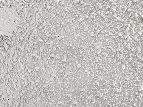 Background of uneven white acoustic wall texture with abstract grain patterns accentuates the modern industrial aesthetic. Close-up of handmade popcorn ceiling has dramatic shadows for decoration.