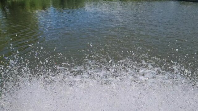 Close-up of water splashing from a paddle wheel aerator in a freshwater fish pond. Aquaculture oxygenation system creating bubbles, foam and surface turbulence for fish farming