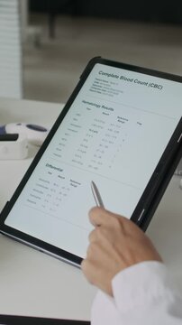 Vertical video of unrecognizable female doctor pointing at complete blood count test results on digital tablet. Footage is ideal for medical software ads or online healthcare services
