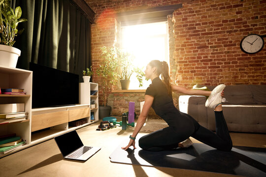 Woman stretching quadriceps on mat during online home workout. Concept of post-workout recovery, muscle flexibility, injury prevention, mobility improvement and virtual fitness coaching sessions.