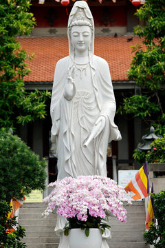 Guan Yin statue stands tall at Vinh Nghiem Buddhist Pagoda in Ho Chi Minh City, Vietnam, surrounded by flowers and flags