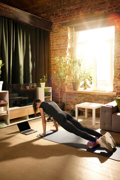 Woman holding plank with feet on foam roller during home training. Concept of core stability, advanced bodyweight exercise, balance control, functional strength and online fitness training programs.