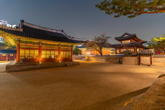 View of Deoksugung Palace at dusk during autumn in Jung District, Seoul, South Korea with illuminated buildings and trees