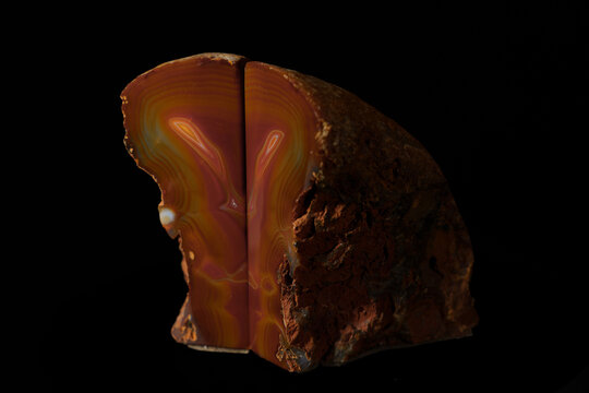 Sliced agate stone reveals vibrant orange and brown banded patterns. Dark background highlights polished cross-section. Natural mineral texture with rough outer edge.