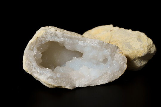 Geode with crystal interior and rough outer shell. Black background enhances mineral details. Smooth, white crystals form inner chamber.