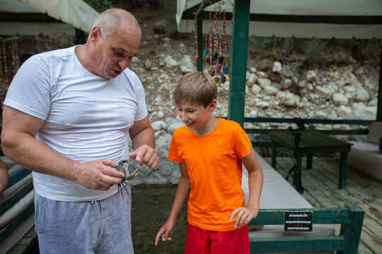 Dad shows his son crabs on the shore of a lake on a summer day against the backdrop of trees and tents