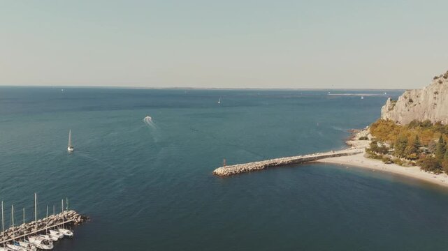 Horizontal 2.7K 60fps drone video flying forward over Sistiana Bay, Italy, revealing the deep blue Adriatic sea, boats, and steep cliffs