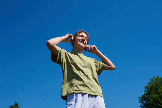 Young teen enjoys music outdoors under a clear blue sky