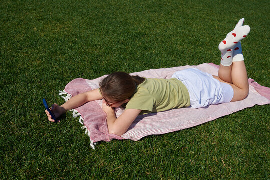 Girl lying on grass looking at phone in sunny park