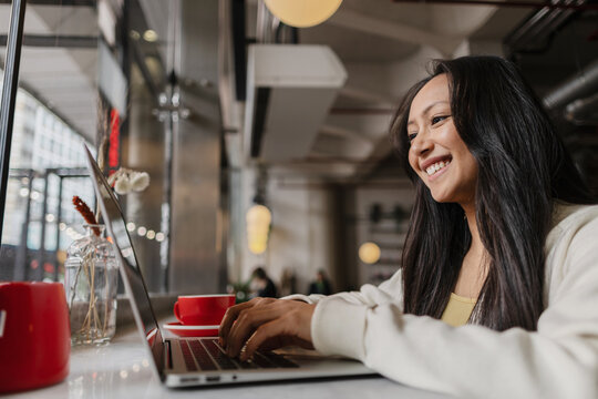 Asian Woman actively working remotely on laptop in cafe