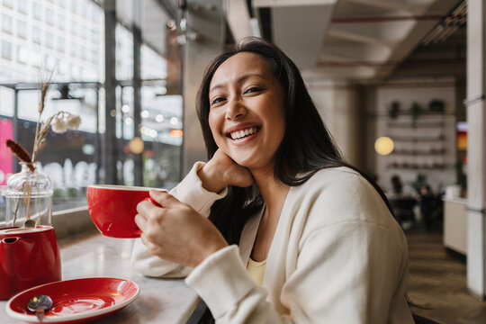 Asian Woman enjoying coffee beverage and smiling in cafe