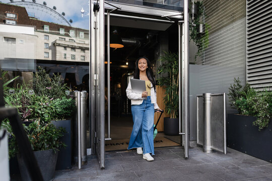 Woman leaving a building with luggage and laptop