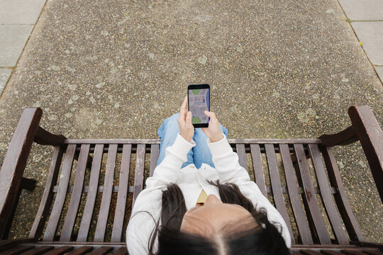 Woman using smartphone mapping application from park bench
