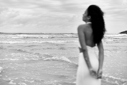 Woman contemplating ocean waves on beach in black and white
