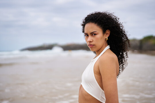 Young woman confidently standing on a beach with curly hair