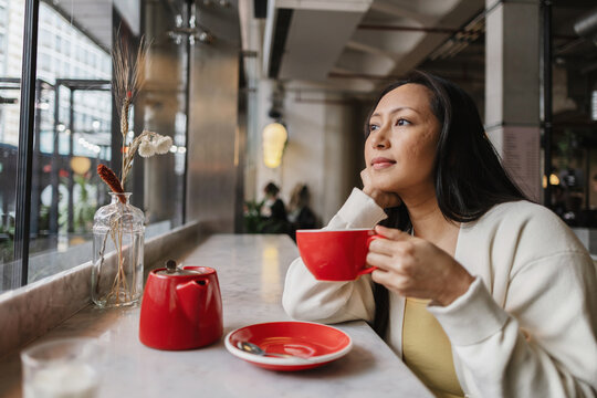 Asian Woman contemplating urban lifestyle while drinking coffee
