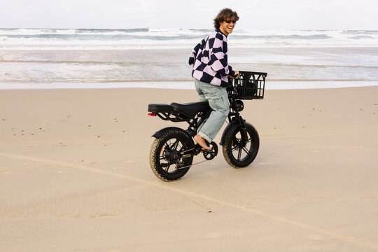 Barefoot man riding electric bike along ocean beach