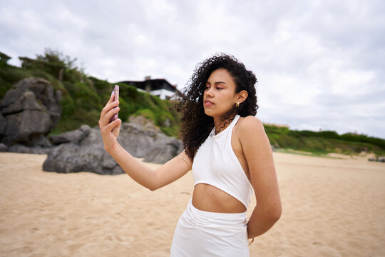 Young woman taking selfie on sandy beach with smartphone