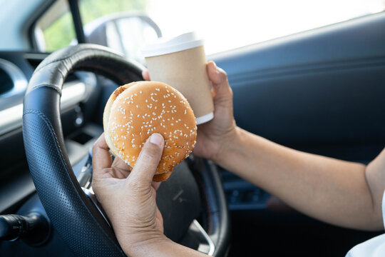 Asian woman driver hold and eat hamburger in car, dangerous and risk an accident.