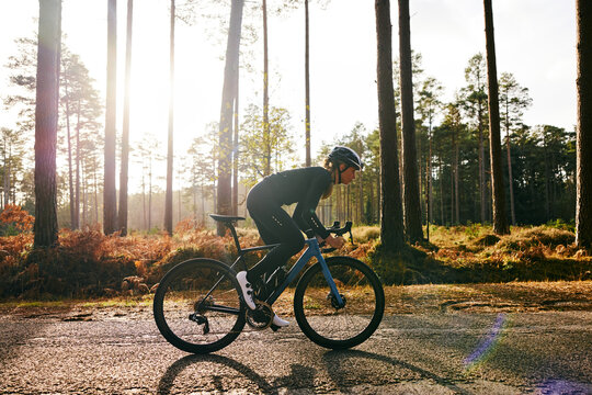 Female Cyclist Training Fast Through Woodland With Sun Flare