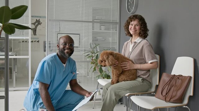 Portrait of African American middle aged male veterinarian and Caucasian young adult woman holding poodle dog smiling at camera. Video suitable for veterinary clinic marketing and pet care promos