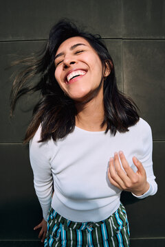 Joyful woman laughing in sunlight against urban wall