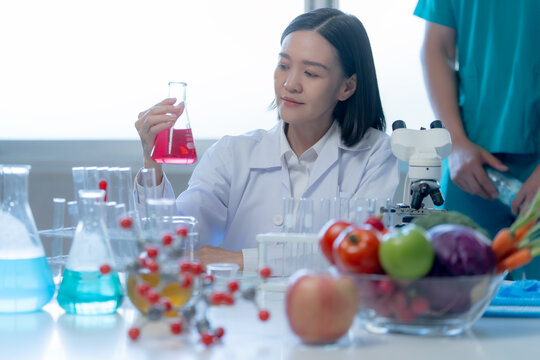Professional female scientist examining a laboratory sample beside fresh fruits and vegetables representing nutrition science food safety and healthcare innovation.
