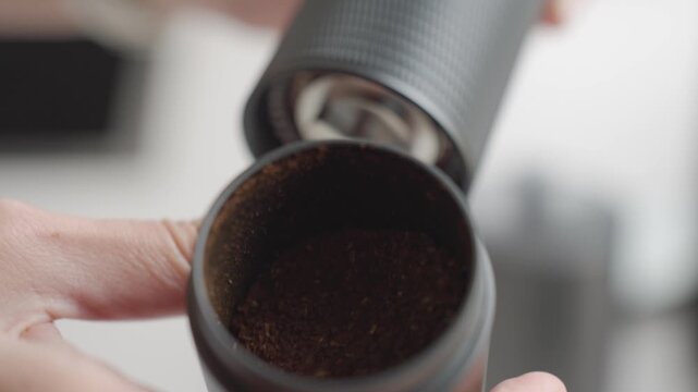 Woman unscrews bottom of manual coffee grinder and shows ground coffee