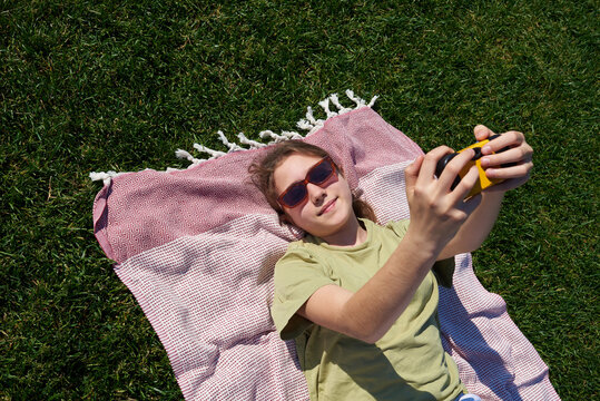 Teen girl takes a selfie while lying on a blanket in the grass 
