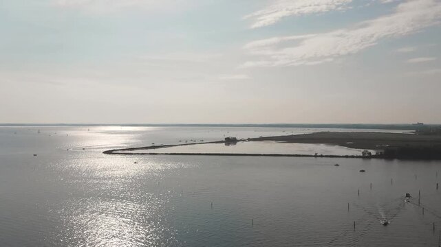 Aerial 2.7K 60fps drone shot of Villaggio del Pescatore coast near Trieste, Italy, with bright sun reflections on the sea water and moving boats at sunset