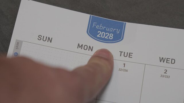 finger pointing at February 2028 planner page close up for scheduling and monthly planning concept