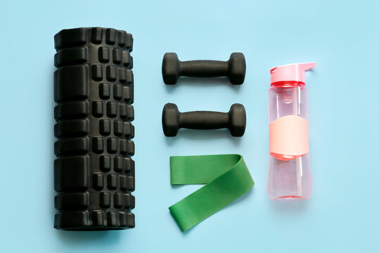 Top view of muscle massage roller,black dumbbells,elastic resistance band and water bottle. Sport and fitness concept