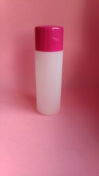 Blank cosmetic plastic bottle mockup with pink cap on pastel pink background, skincare packaging template, copy space.