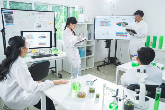 Laboratory scientist research team chemistry experiment presentation data chart microscope, group reviews report with glassware, green liquid, white coat, focused collaboration in bright lab