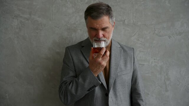 Handsome and successful businessman in stylish suit holding glass whiskey while sitting on the stool