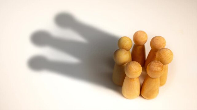 Wooden doll figures standing in a circle casting a shadow of a king crown, representing team collaboration, corporate leadership, power of teamwork, talent management, and authority concept.