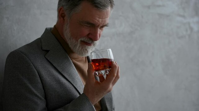 Handsome and successful businessman in stylish suit holding glass whiskey while sitting on the stool