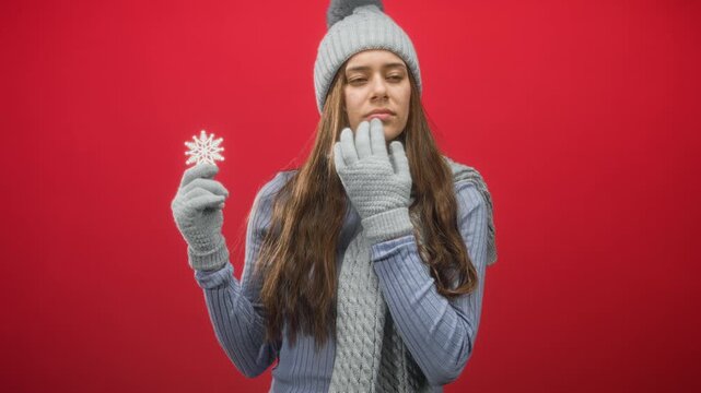 Woman holding snowflake with gloved hand and touching chin with other gloved hand in studio; contemplative.