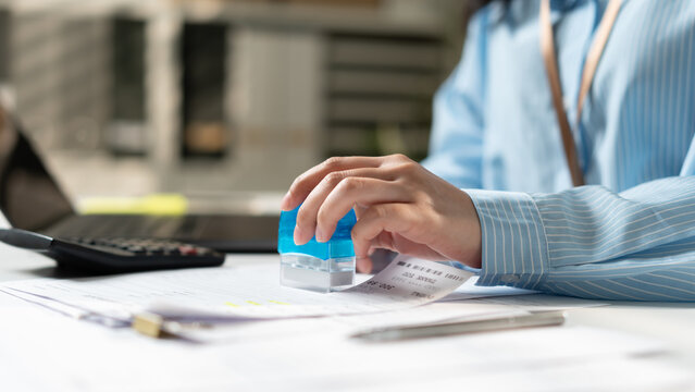 Close up of businesswoman stamping document with rubber stamp at office desk. Accountant approving invoice receipt, financial tax or agreement concept.