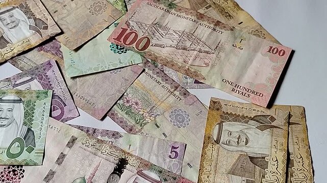 A close-up of Saudi Riyal (SAR) banknotes arranged on a white background, showing various denominations.