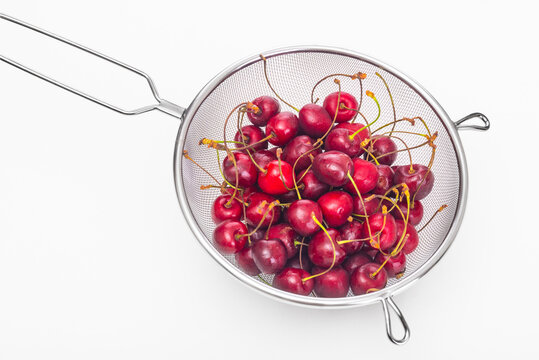 Ripe cherries in a colander on a white background