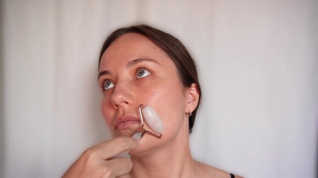 Woman using a stone facial roller for face massage and daily skincare against a neutral background