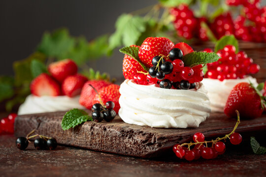 Pavlova dessert with fresh berries and mint on an brown vintage table.