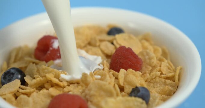 Milk pouring with splash into cornflakes with berry breakfast cereal bowl healthy morning meal