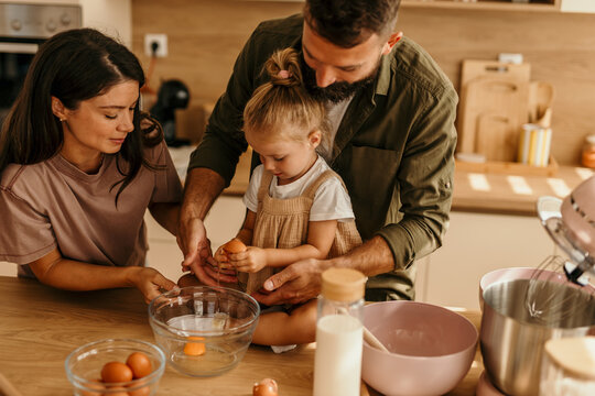 Family baking together in kitchen, child cracking egg