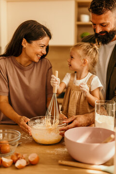 Happy family baking together, child whisking ingredients in kitchen