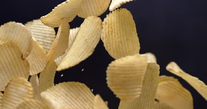 Ridged potato chips falling in slow motion on black background
