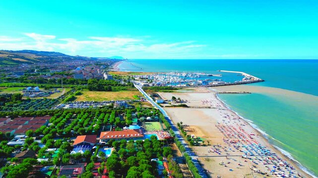 Wonderful aerial truck left pan right shot between Marina Palmense and Porto San Giorgio, the vast expanses of Adriatic Sea washing the minutely sandy beach with parasols and bathers under sunny skies