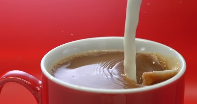 Cream pouring into coffee in a red mug, super slow motion