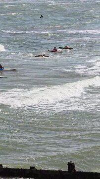 Vertical panning shot of a surf school session on the beach at Cromer, North Norfolk, following surfers across the waves with the town&rsquo;s scenic coastline in the background.